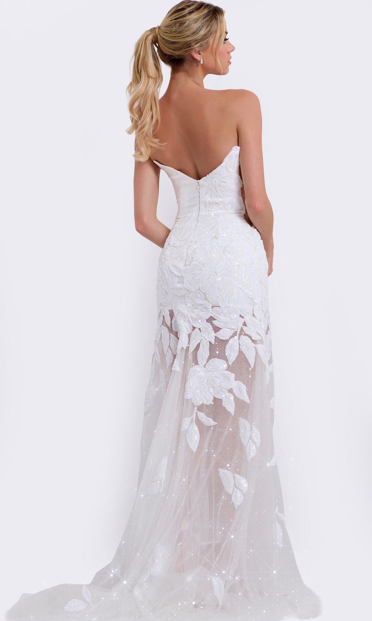 A blonde woman in a ponytail is seen from the back wearing the Long Prom Dress: Jovani 44437, which features a strapless design, floral lace details, and a sheer train, set against a plain background.